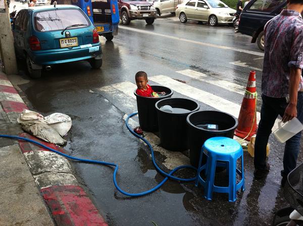 Child inside a black barrel with blue hose, wet street during rain