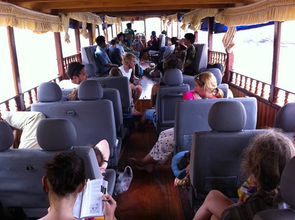 Passengers seated on grey seats inside a wooden boat underway