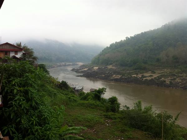 Muddy river in morning mist, boats on shore, wooden houses and green hills