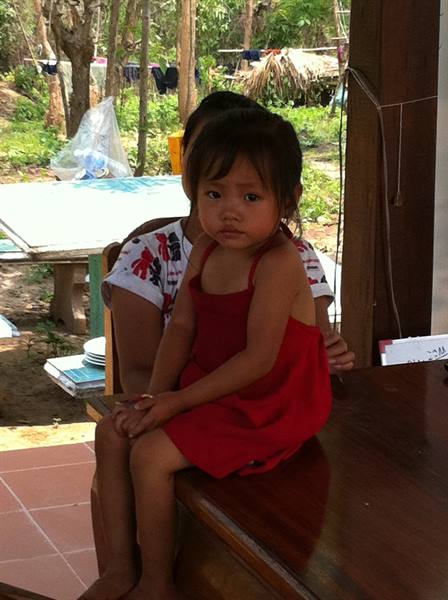 Little girl in red dress sitting on wooden table, woman behind her