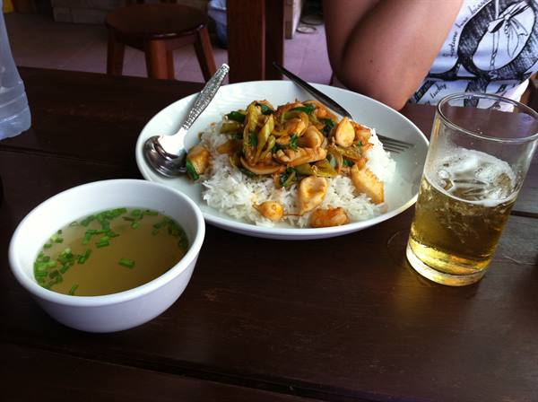 Plate of rice with squid and vegetables, soup and beer on wooden table