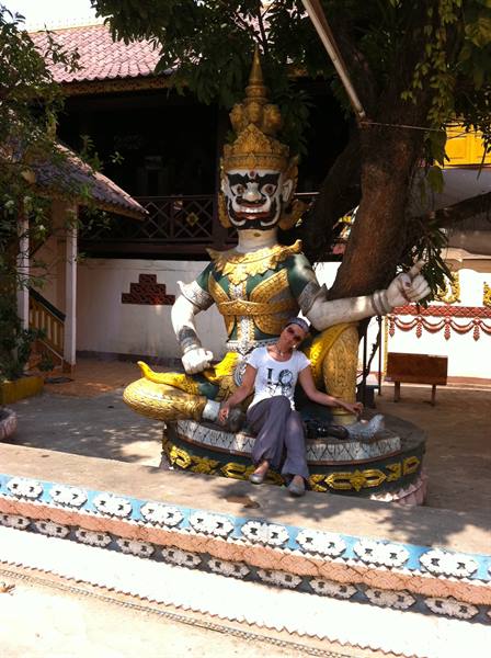 Tourist sitting beside a painted Thai demon statue under a tree shade