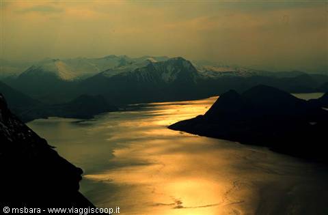 Golden fjord waters winding between snowy mountains under an amber sky