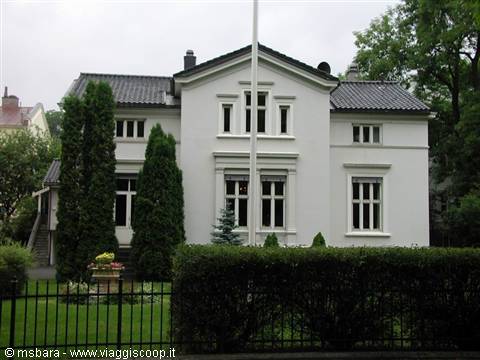 White villa with dark roof and boxwood hedge behind iron fence