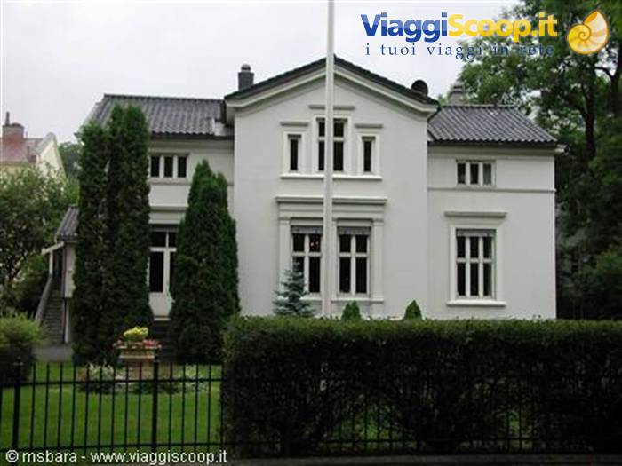 White villa with dark roof and boxwood hedge behind iron fence