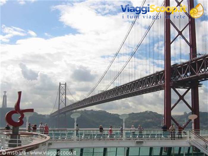 Tourists on ship deck beneath the 25 de Abril Bridge in Lisbon