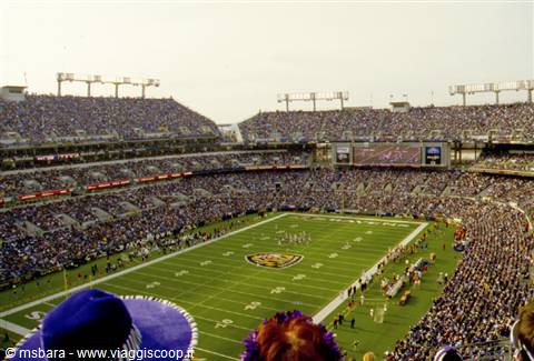 Football stadium packed with fans, green lit field with game underway