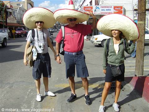 Three tourists wearing large sombreros walk along a town street