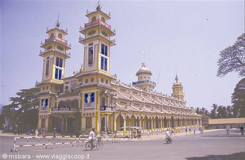 Pastel twin-towered cathedral, cyclists on the road, bright light