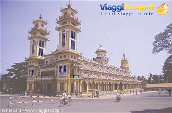 Pastel twin-towered cathedral, cyclists on the road, bright light