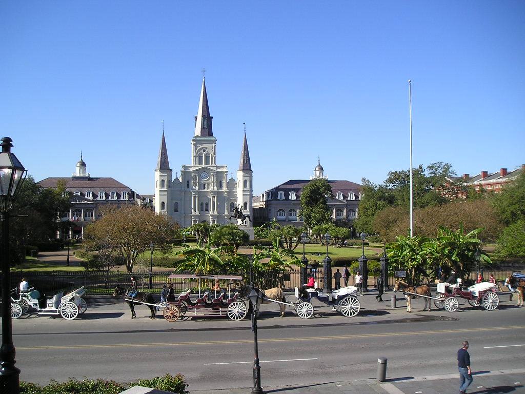 St. Louis Cathedral in New Orleans, horse-drawn carriages passing under a blue sky