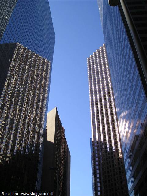 Glass skyscrapers with reflective facades against blue sky, seen from below