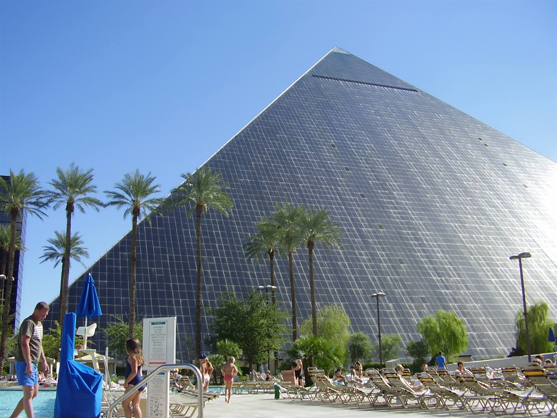 Black glass pyramid of the Luxor hotel, palm trees and people by the pool