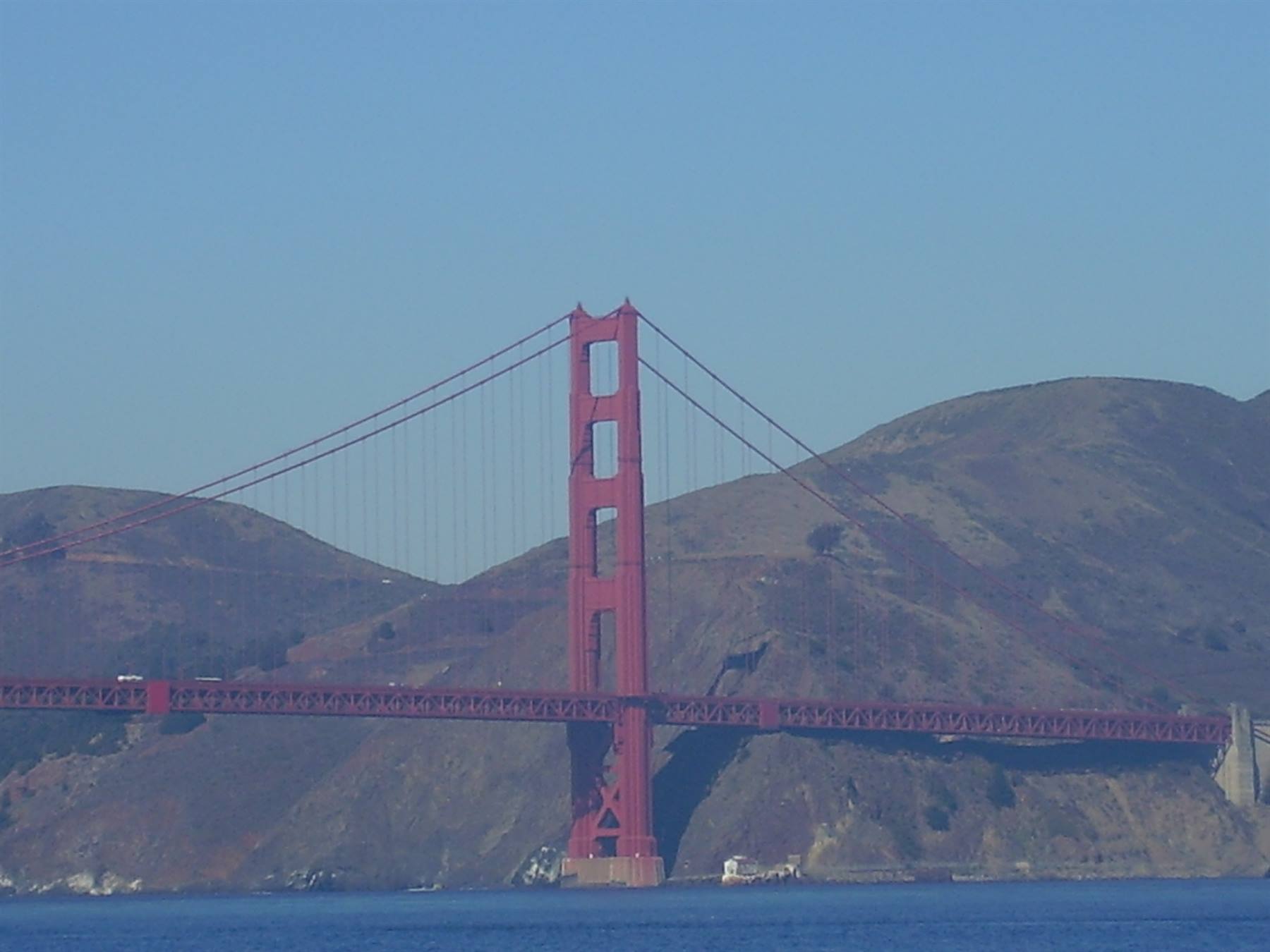 Red tower of the Golden Gate Bridge above the bay, bare hills behind