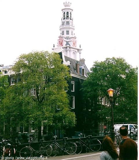 Westerkerk bell tower above trees, parked bikes and pedestrians in Amsterdam
