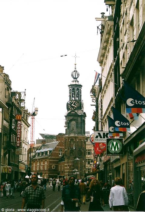 The Munttoren tower rises over a busy Amsterdam street among shop signs