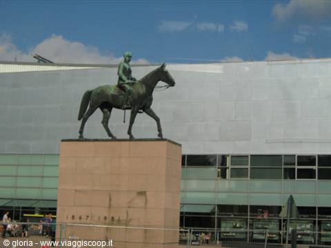 Bronze equestrian statue on stone pedestal in front of a modern building