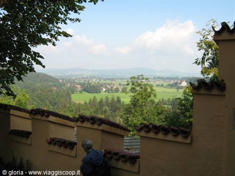 Weathered walls with exposed tiles above green fields and hills under white clouds
