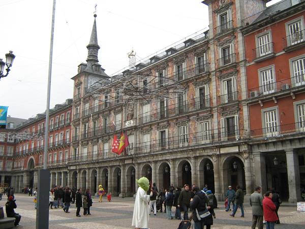 Plaza Mayor in Madrid: painted red facades, Spanish flags, tourists and a living statue