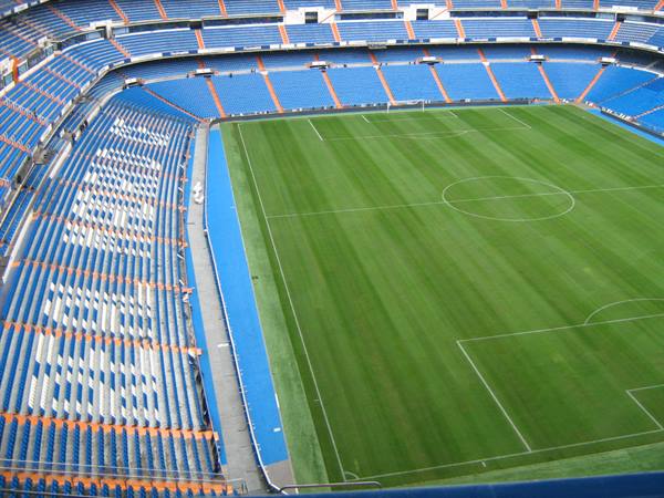 Santiago Bernabéu stadium, empty blue stands and striped grass pitch in daylight
