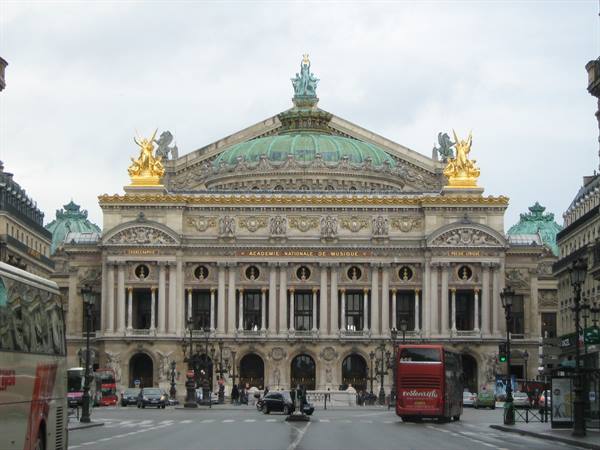 The Palais Garnier in Paris, stone facade with green dome and golden statues, city traffic