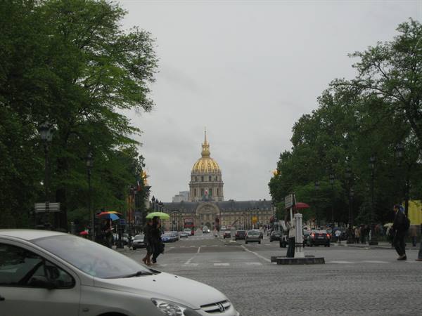 People with umbrellas cross the esplanade toward the golden Invalides dome, Paris