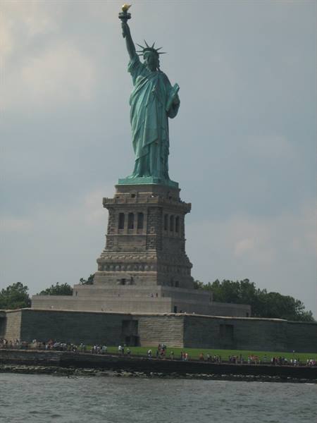 Copper Statue of Liberty on stone pedestal, visitors along the waterfront