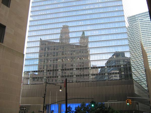 Glass office building reflecting historic towers and skyscrapers above a city street