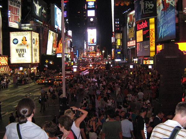 Crowd among glowing billboards in Times Square at night, yellow taxis on the street
