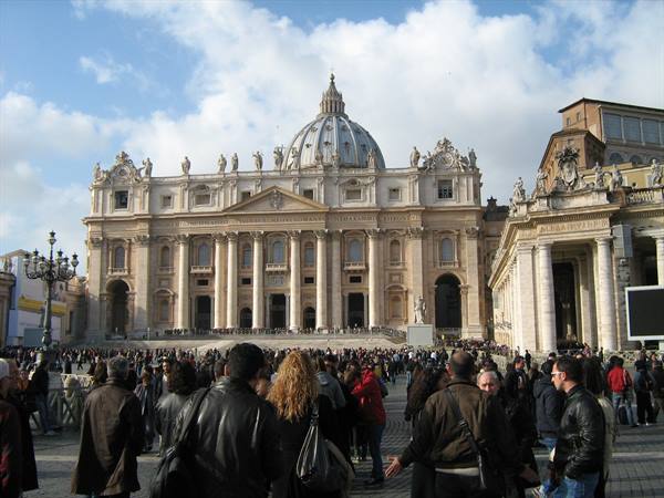 Crowds of tourists fill St. Peter's Square before the Basilica under white clouds