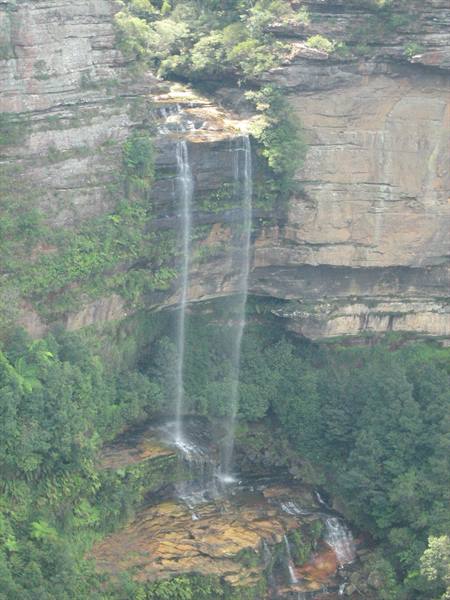Waterfall plunging down sandstone cliffs among ferns and green trees