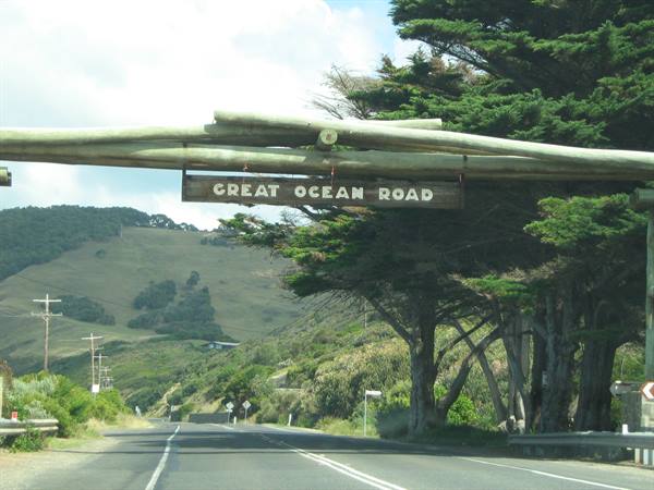 Wooden log sign marks the Great Ocean Road entrance among green hills and eucalyptus trees