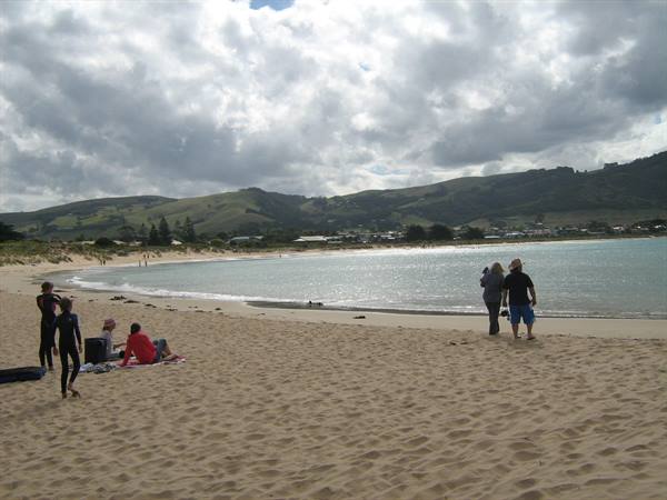 Families on sandy beach in front of turquoise bay and green cloudy hills