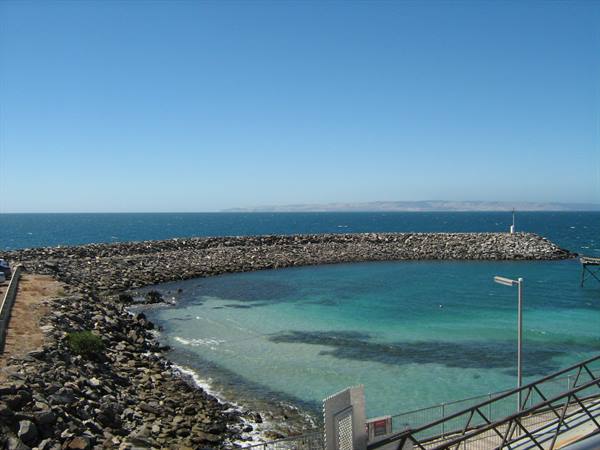 Rock breakwater around turquoise water, lampposts and metal railing under blue sky