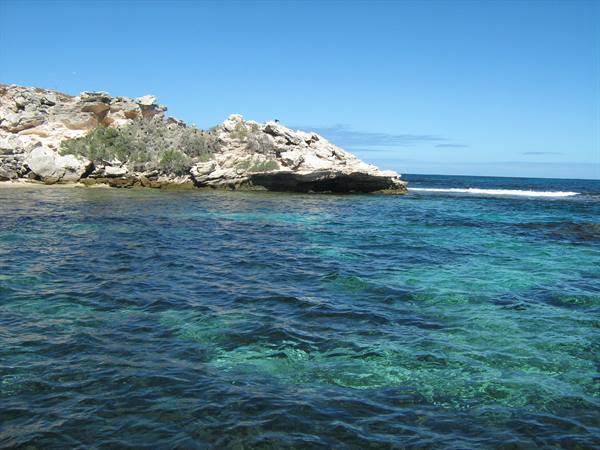 Sandy limestone rocks over turquoise sea, white waves under blue sky