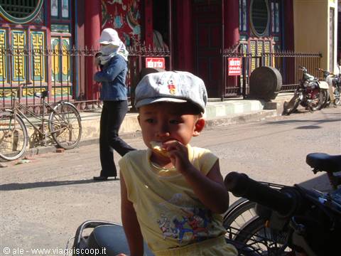Child in cap eating on the street in front of a Vietnamese temple