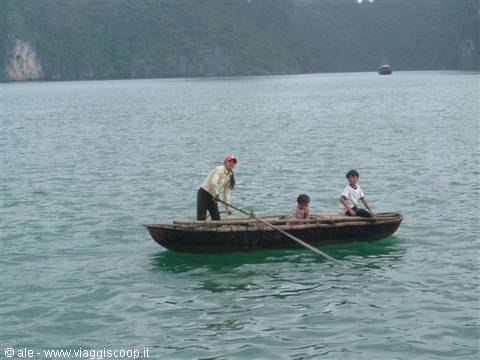 Wooden boat with rower and children glides through Ha Long Bay