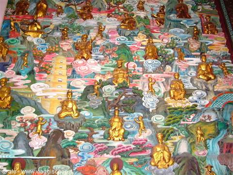 Wall relief with dozens of golden Buddha statues among painted clouds in a temple