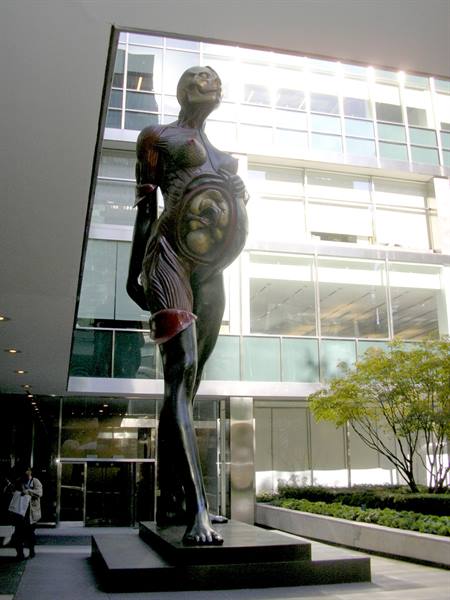 Bronze statue of pregnant woman with visible fetus before glass building