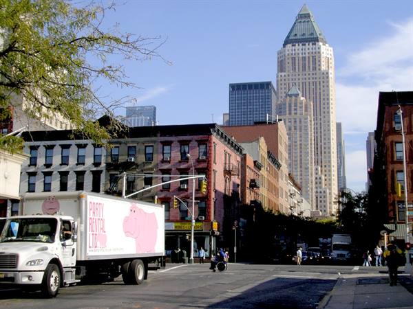 White truck with pink hippo at intersection, brick houses and skyscrapers behind