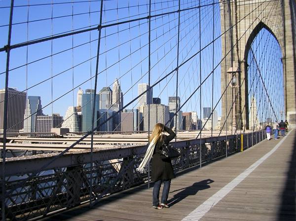 Woman photographing Manhattan skyline from Brooklyn Bridge walkway