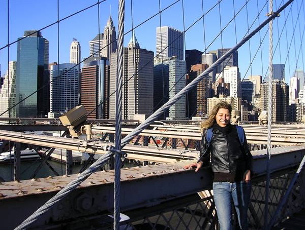 Smiling woman on Brooklyn Bridge, Manhattan skyscrapers under the sun
