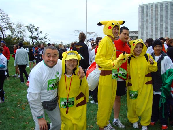 Runners in yellow Pikachu costumes pose with race bibs on crowded grass