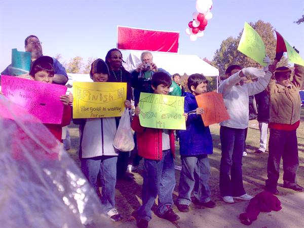 Kids holding colorful signs at an outdoor race finish line