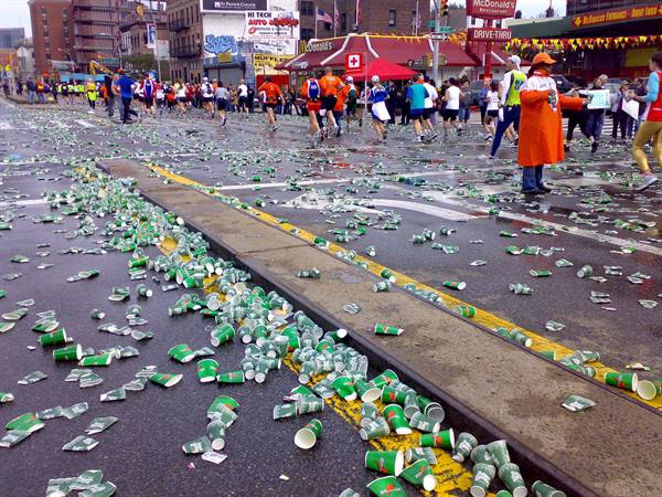 Marathon runners pass discarded paper cups on wet city asphalt