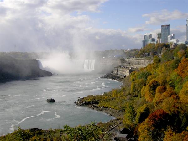 Niagara Falls shrouded in mist, autumn trees and skyscrapers behind