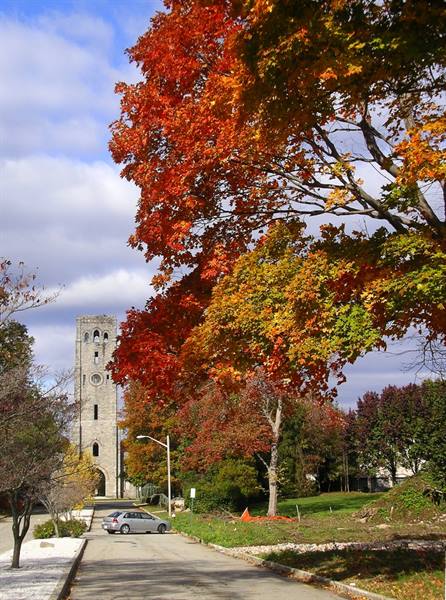 Stone bell tower amid red autumn maples, street with parked car