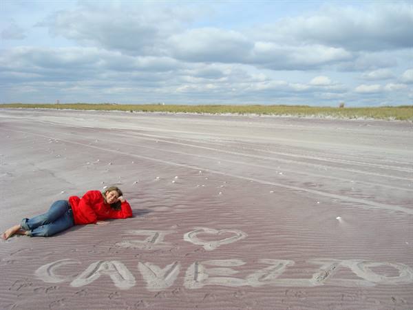 Woman in red jacket lying on purple sand at Cavello beach, writing in the sand