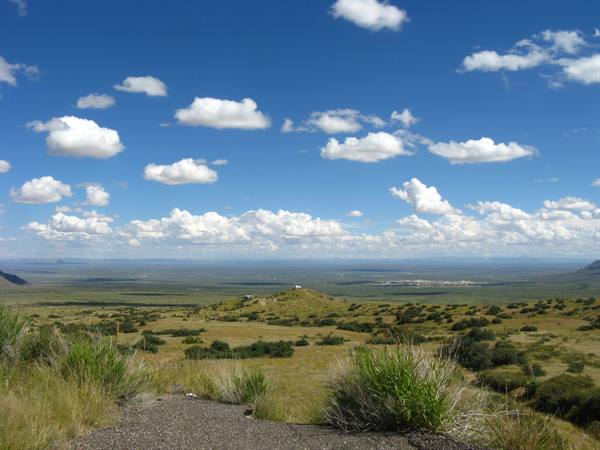 Sentiero ghiaioso tra arbusti verdi verso la vallata, nuvole bianche sul cielo azzurro