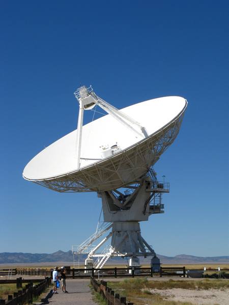 Antenna radio bianca del Very Large Array, due turisti passeggiano sotto